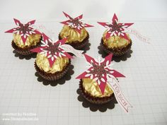 four chocolate cupcakes decorated with red and white flowers on a sheet of paper