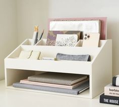 a white desk organizer with books, magazines and pens on it next to a stack of notebooks