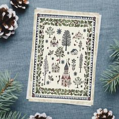 a christmas card with trees, houses and pine cones on the table next to it