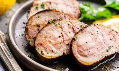 sliced meat on a plate with lemons and parsley