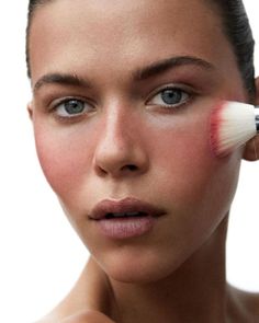 a woman is holding a brush in her hand and applying it on her face with makeup