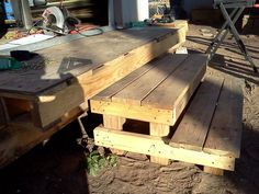 a wooden bench sitting on top of a dirt ground next to a table and chairs