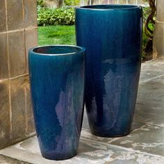 two large blue vases sitting next to each other on a stone patio area with grass in the background