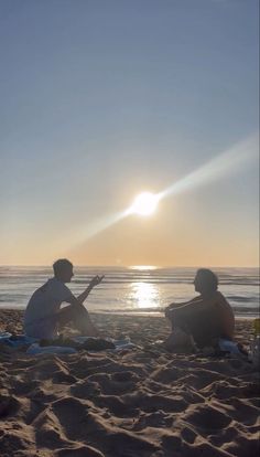 two people sitting on the beach at sunset