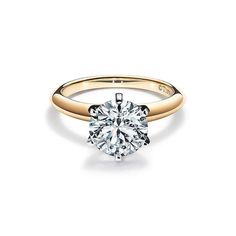 a yellow gold engagement ring with a round cut diamond in the center, on a white background