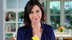 a woman holding a yellow flower in her right hand and looking at the camera with an intense smile on her face