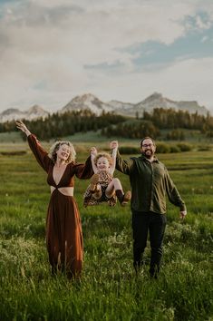 a man and woman are standing in the grass with their arms up as they hold an infant