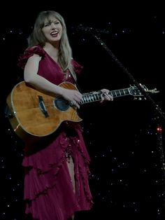 a woman in a red dress holding a guitar and singing into a microphone on stage