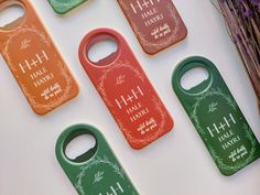 four bottle openers with names on them sitting next to some dried flowers and twigs