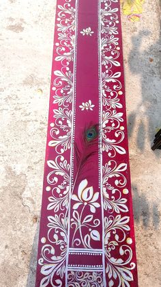 a long red table runner with white designs and a peacock feather on the top, along with other decorative items