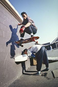 two people are doing tricks on their skateboards against a wall with the shadow of a man