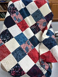 a red, white and blue quilt sitting on top of a wooden chair next to a book shelf