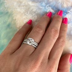 a woman's hand with pink nail polish holding a diamond ring and two wedding bands