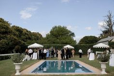 a group of people standing in front of a pool next to some white umbrellas