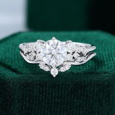 a diamond ring sitting on top of a green velvet cushioned surface, with the center stone surrounded by smaller round diamonds