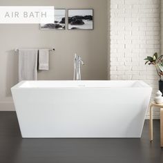 a white bath tub sitting in a bathroom next to a wooden table and two pictures on the wall