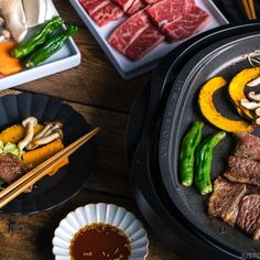 an assortment of meats and vegetables being cooked on a grill with chopsticks