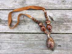 Nature made a seashell full of style!  The Tiger Cowry Shell is perfect for the animal print craze!  The ceramic beads come from the NC mountains.  This statement piece is so unique and perfect for your Fall outfits!  It is finished with tan suede for great comfort! Handmade Brown Bohemian Shell, Bohemian Brown Shell As Gift, Handmade Bohemian Brown Shell, Bohemian Brown Shell, Cowry Shell, Nc Mountains, Boho Glam, The Tiger, Tan Suede