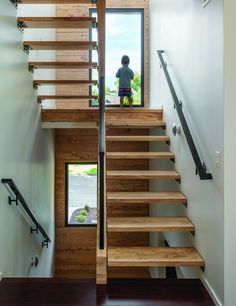 there is a person standing at the top of some stairs in this house, looking out onto the street