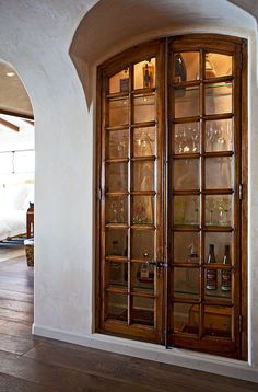 an arched glass door with wine glasses on it in front of a white wall and wood floor