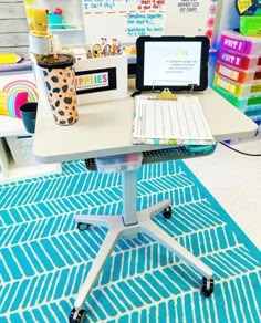 a laptop computer sitting on top of a white desk next to a blue and white rug