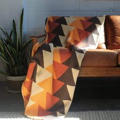 an orange and brown blanket sitting on top of a couch next to a potted plant