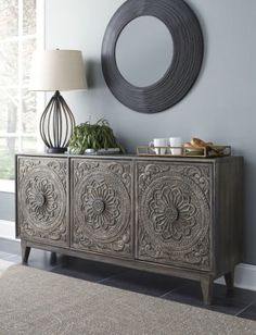 an ornately decorated sideboard stands in front of a blue wall with a round mirror above it