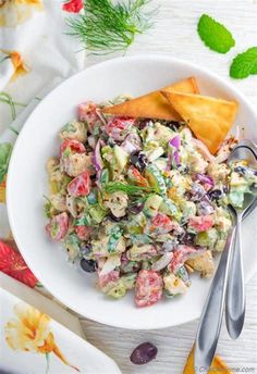 a white bowl filled with salad next to two silver spoons on top of a table