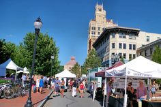 many people are walking down the street at an outdoor market