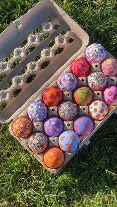 an egg carton filled with painted eggs on top of green grass in the sun