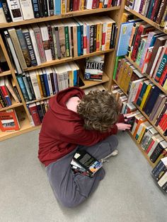 a person sitting on the floor in front of a book shelf with many different books