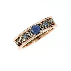 a gold ring with blue stones and filigrees on the sides, set against a white background