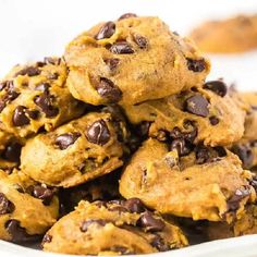 chocolate chip cookies stacked on top of each other in a white bowl with more cookies behind it