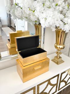 a gold vase with white flowers in it sitting on a table next to other boxes