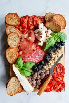 an assortment of breads, meats and vegetables on a cutting board