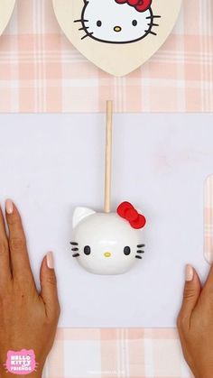 two hands are holding a hello kitty lollipop holder on a pink and white checkered tablecloth