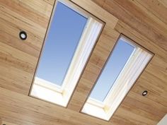 a bed sitting under two windows in a bedroom next to a wooden wall and ceiling