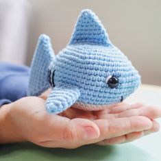 a hand holding a small blue crocheted shark