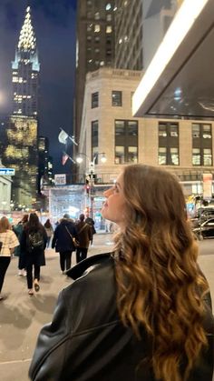 a woman standing in the middle of a city at night with her head tilted back