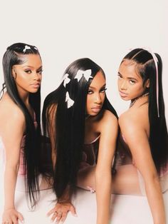 three women with long black hair sitting next to each other on a white surface,