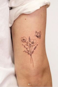 a small flower tattoo on the side of a woman's right leg, with two butterflies flying over it