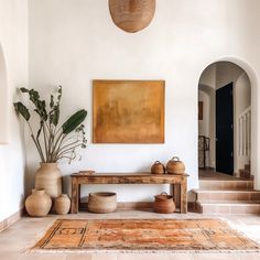 a large painting hanging on the wall next to a wooden bench and potted plant