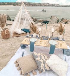 a table set up on the beach for an outdoor dinner party with candles and place settings