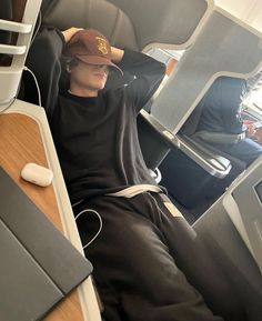 a man sitting on an airplane with headphones in his ears and wearing a hat