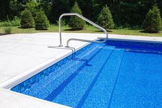 an empty swimming pool surrounded by trees and bushes in the back ground, with a metal hand rail