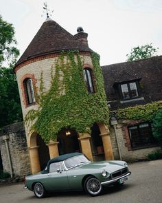 an old green car parked in front of a building with ivy growing on it's side