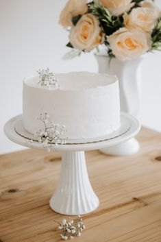 a white cake sitting on top of a wooden table next to a vase with flowers