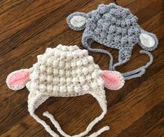 two crocheted sheep hats sitting on top of a wooden floor