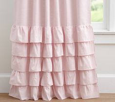 a pink shower curtain with ruffles hanging from it's side in front of a window