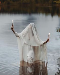 a woman with two candles in her hands standing in the water, holding an object